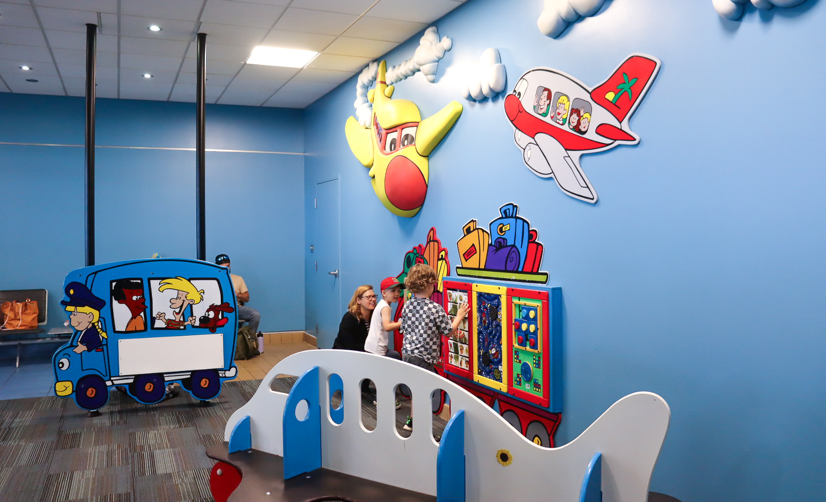 Two children and a woman are playing with aviation-themed equipment in a blue room at the airport.