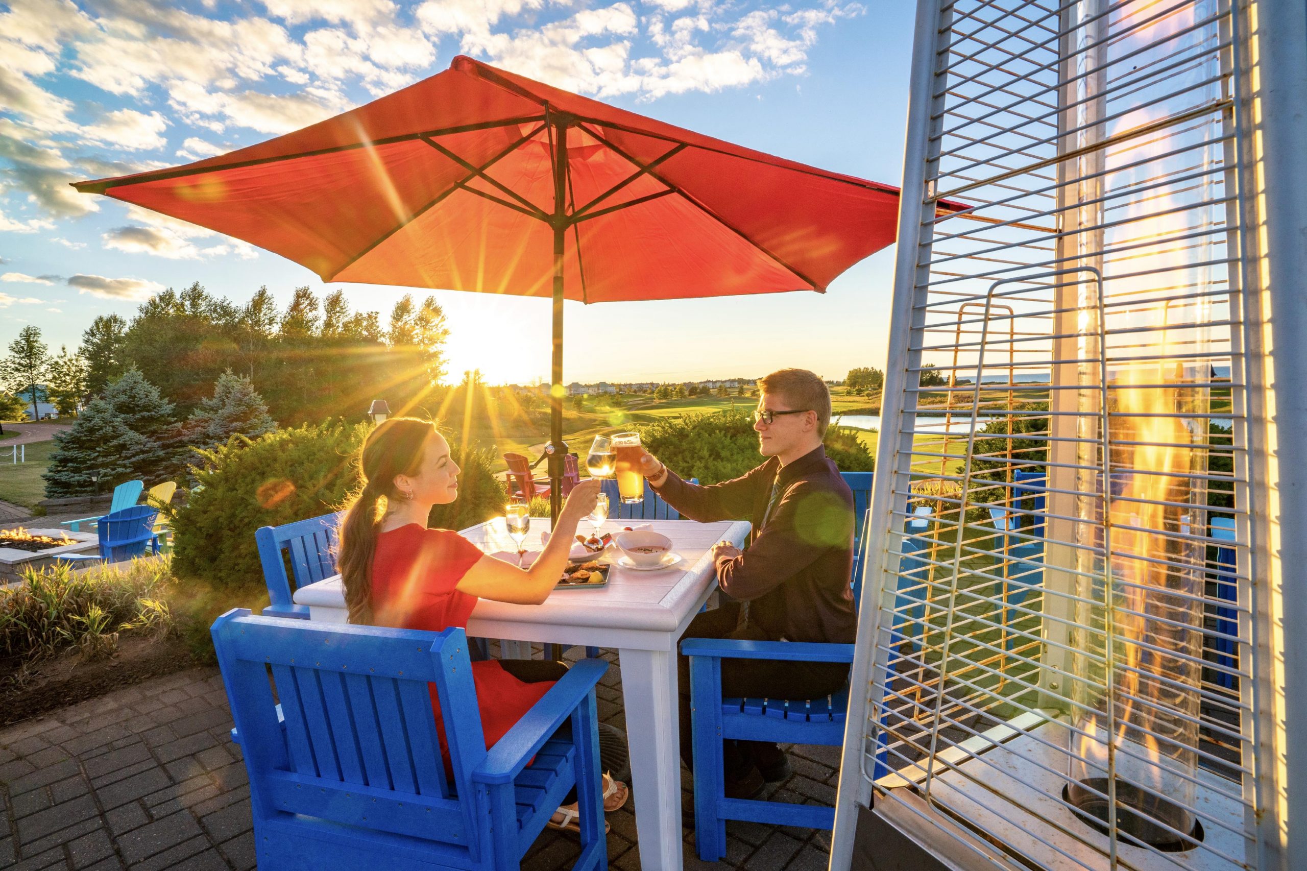 A father and daughter clinking glasses at a patio table as the sun sets