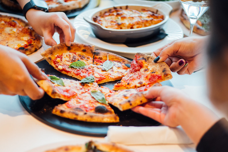 Two people pick up slices of pizza from a tray.